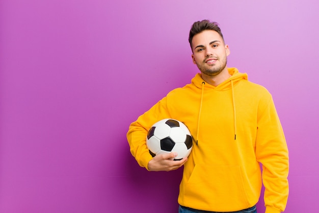 Joven hispano con un balón de fútbol contra púrpura