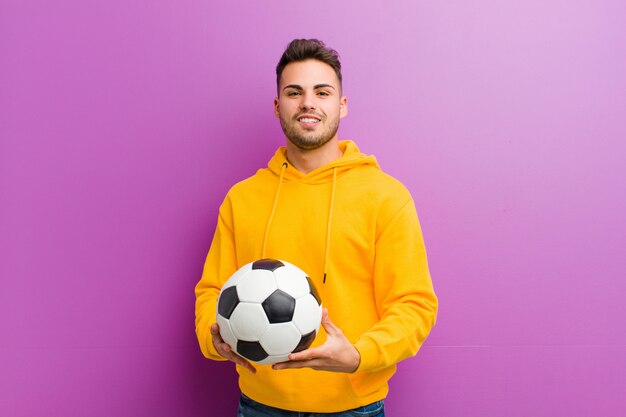 Joven hispano con un balón de fútbol sobre fondo morado