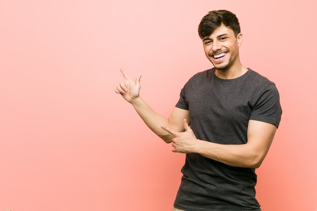 Joven hispano casual señalando con el dedo índice a un espacio de copia, expresando emoción y deseo.