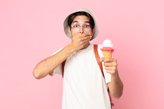 Joven hispano cubriendo la boca con las manos con un sorprendido y sosteniendo un helado