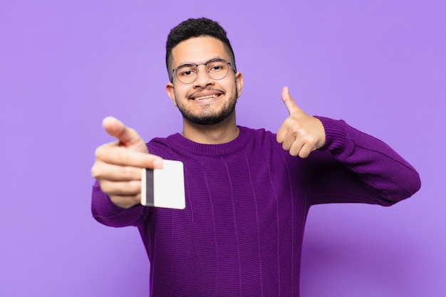 Joven hispano con expresión feliz y sosteniendo una tarjeta de crédito