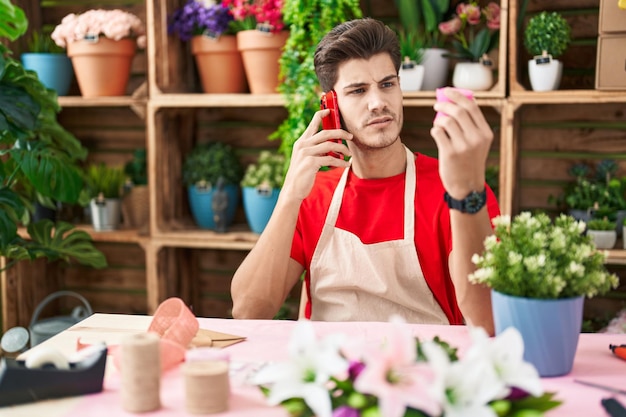 Joven hispano florista hablando por teléfono inteligente con encaje de regalo en la floristería