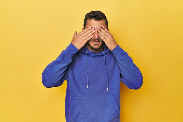 Foto joven hispano de fondo amarillo asustado cubriéndose los ojos con las manos
