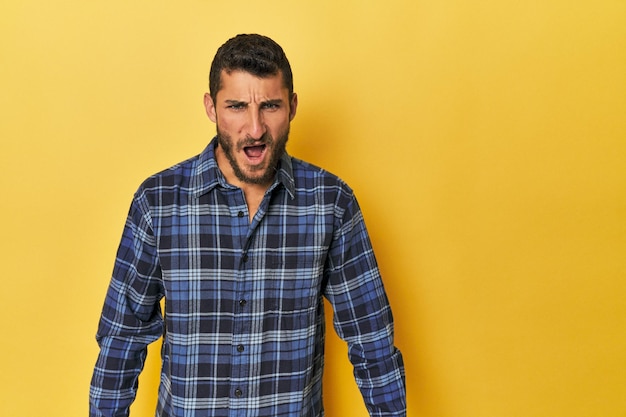 Foto joven hispano en fondo amarillo gritando muy enojado rabia concepto frustrado