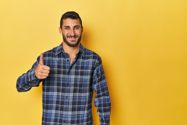 Joven hispano de fondo amarillo sonriendo y levantando el pulgar hacia arriba