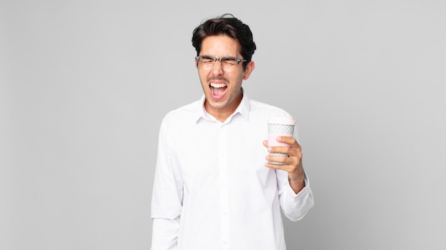 Joven hispano gritando agresivamente, mirando muy enojado y sosteniendo un café para llevar