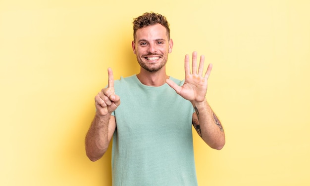 Joven hispano guapo sonriendo y luciendo amigable, mostrando el número seis o sexto con la mano hacia adelante, contando hacia atrás