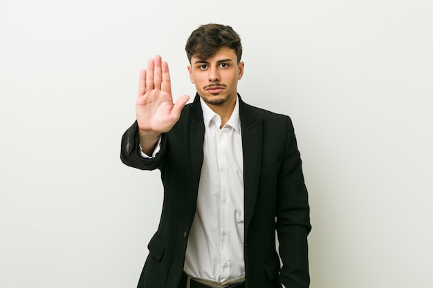 Joven hispano hombre de negocios de pie con la mano extendida que muestra la señal de stop, evitando que.