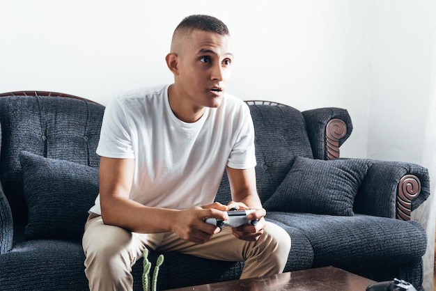 Joven hispano jugando videojuegos sentado en el sofá Copiar espacio Gamer jugando en la consola