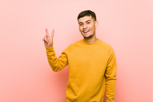 Joven hispano mostrando el signo de la victoria y sonriendo ampliamente.