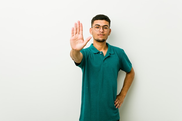 Joven hispano de pie con la mano extendida que muestra la señal de stop, impidiéndole.