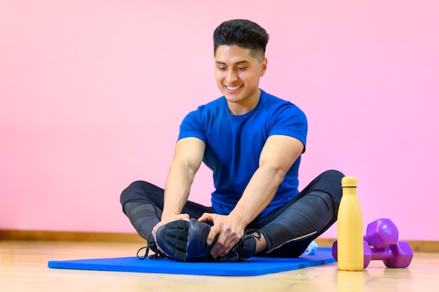 Joven hispano practicando yoga en su colchoneta en el gimnasio sobre fondo rosa.