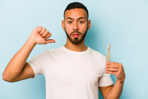 El joven hispano que se cepilla los dientes aislado de fondo azul se siente orgulloso y seguro de sí mismo como un ejemplo a seguir