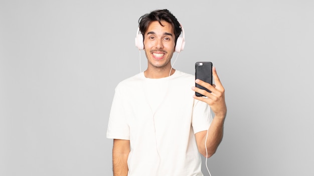 Joven hispano que parece feliz y gratamente sorprendido con auriculares y smartphone