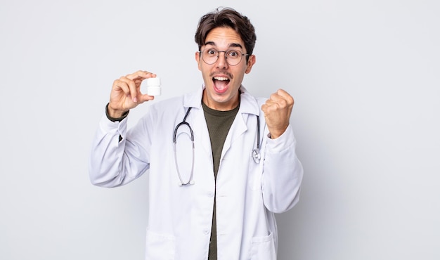 Joven hispano que se siente conmocionado, riendo y celebrando el éxito del médico con el concepto de botella de pastillas