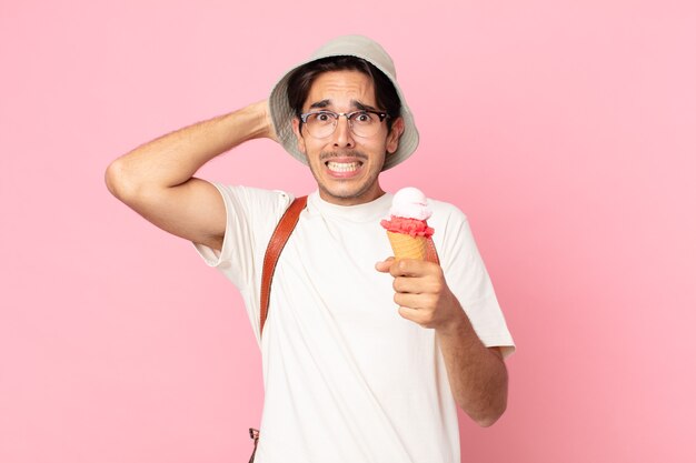 Joven hispano que se siente estresado, ansioso o asustado, con las manos en la cabeza y sosteniendo un helado