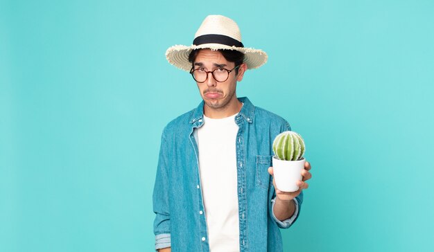 Joven hispano que se siente triste y quejumbroso con una mirada infeliz y llorando y sosteniendo un cactus