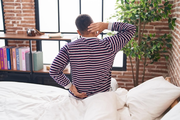 Un joven hispano que sufre de una lesión en la espalda sentado en la cama en el dormitorio