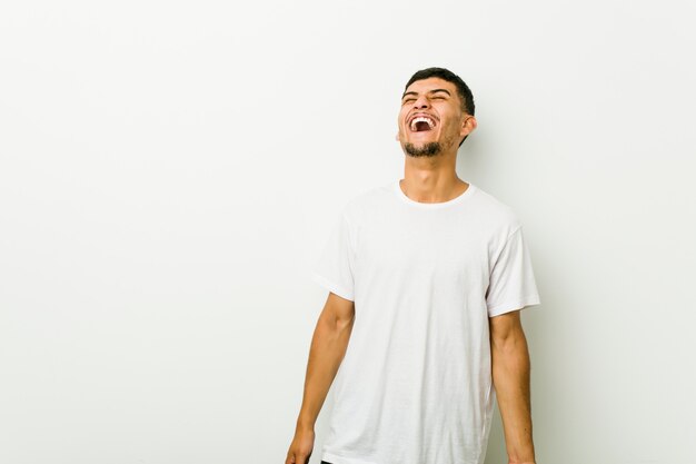 Joven hispano relajado y feliz riendo, cuello estirado mostrando los dientes.