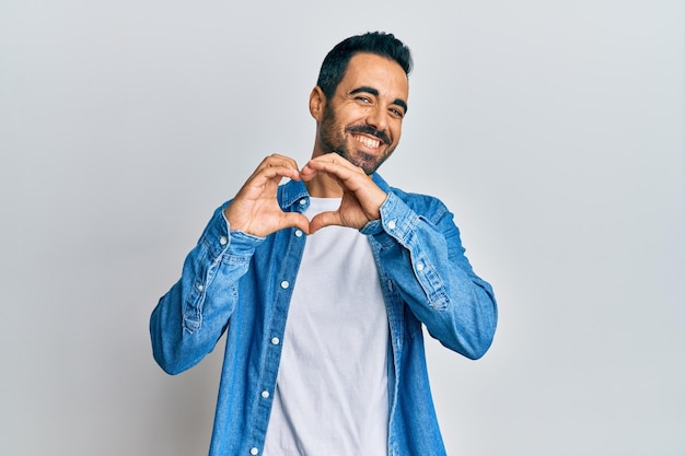 Joven hispano con ropa informal sonriendo enamorado haciendo forma de símbolo de corazón con las manos concepto romántico