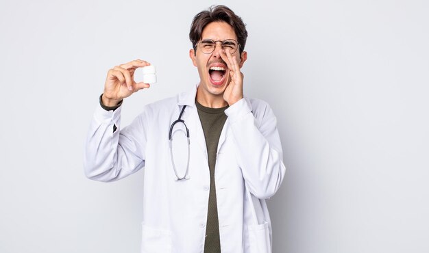 Joven hispano se siente feliz, dando un gran grito con las manos al lado de la boca. médico con concepto de botella de píldoras