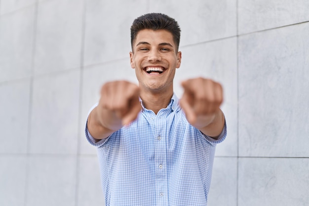 Joven hispano sonriendo confiado apuntando con los dedos a la calle