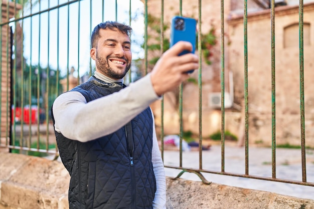 Un joven hispano sonriendo confiado tomando una selfie con el teléfono inteligente en la calle