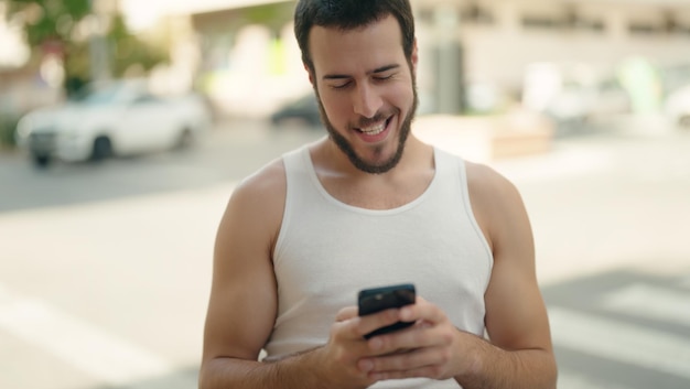 Joven hispano sonriendo confiado usando un teléfono inteligente en la calle