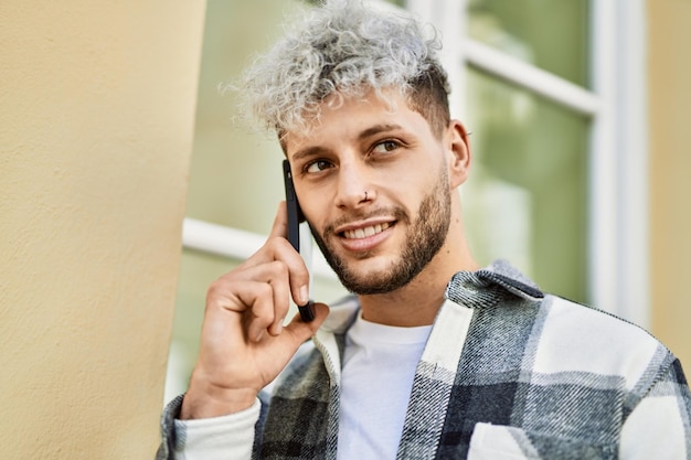 Joven hispano sonriendo feliz hablando de smartphone en la ciudad.