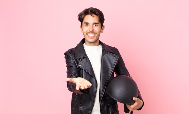 Joven hispano sonriendo felizmente con amable y ofreciendo y mostrando un concepto. concepto de piloto de moto