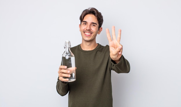 Joven hispano sonriendo y luciendo amigable mostrando el concepto de botella de agua número tres