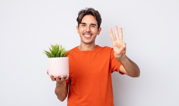 Joven hispano sonriendo y luciendo amigable mostrando el concepto de planta decorativa número tres