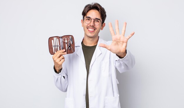 Joven hispano sonriendo y luciendo amigable mostrando herramientas de uñas de podólogo número cinco