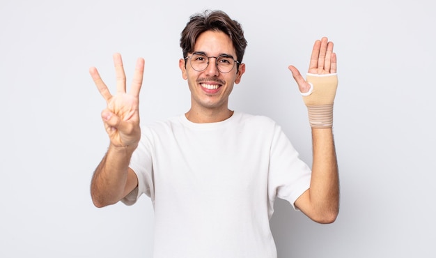 Joven hispano sonriendo y luciendo amigable, mostrando el número tres. concepto de vendaje de mano