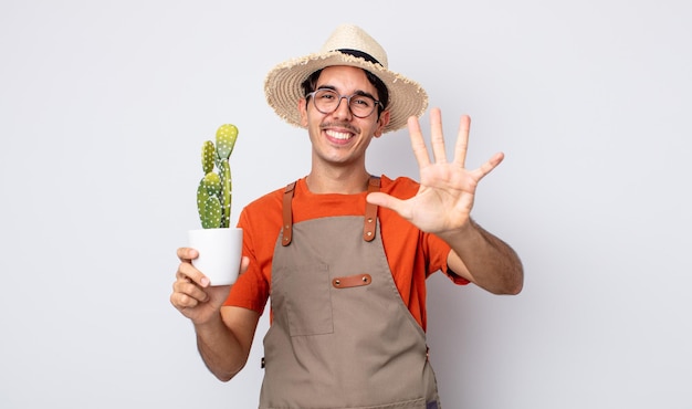 Joven hispano sonriendo y mirando amigable, mostrando el número cinco. jardinero con concepto de cactus