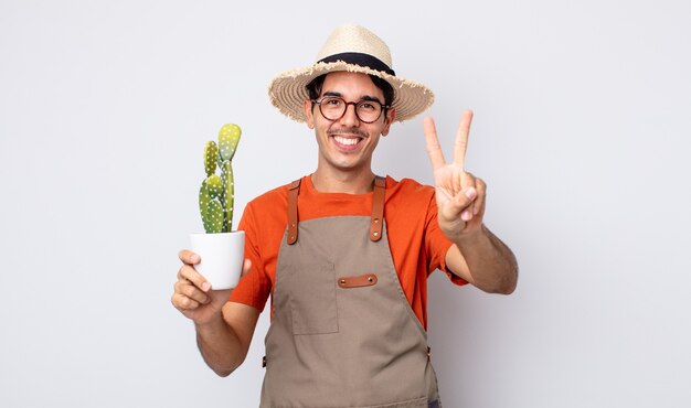 Joven hispano sonriendo y mirando amigable, mostrando el número dos. jardinero con concepto de cactus