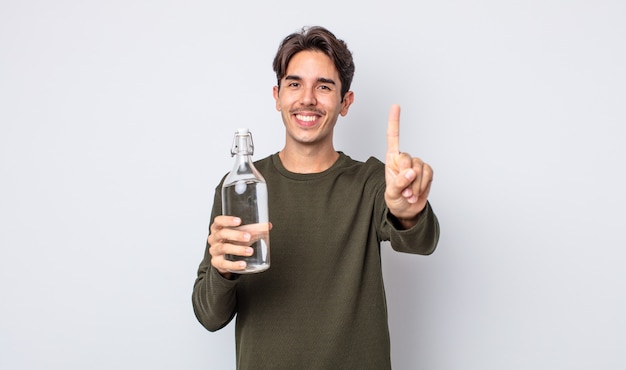 joven hispano sonriendo y mirando amistoso, mostrando el número uno. concepto de botella de agua