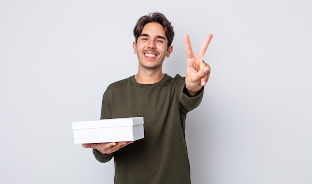 Joven hispano sonriendo y mirando feliz, gesticulando victoria o paz. concepto de caja blanca