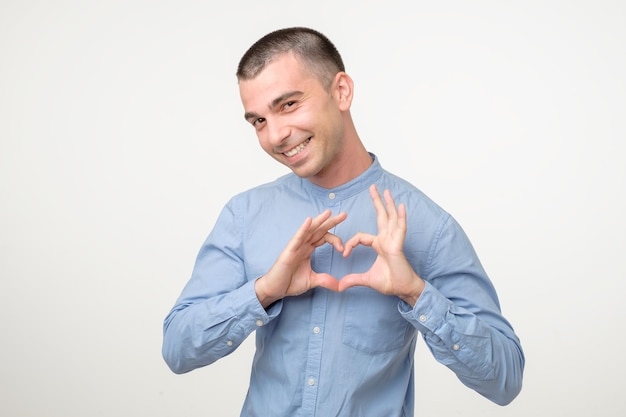 Joven hispano sonriente con camisa azul que muestra el signo del corazón