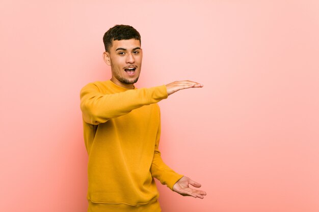 Joven hispano sorprendido y sorprendido sosteniendo un espacio en blanco entre las manos.