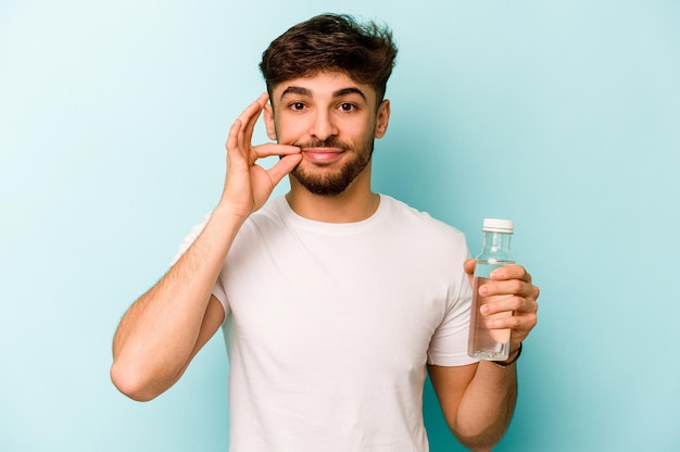 Joven hispano sosteniendo una botella de agua aislada de fondo blanco con los dedos en los labios guardando un secreto