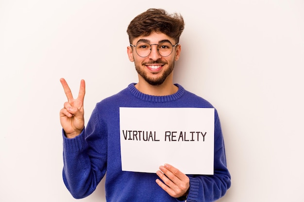 Joven hispano sosteniendo un cartel de realidad virtual aislado de fondo blanco que muestra el número dos con los dedos