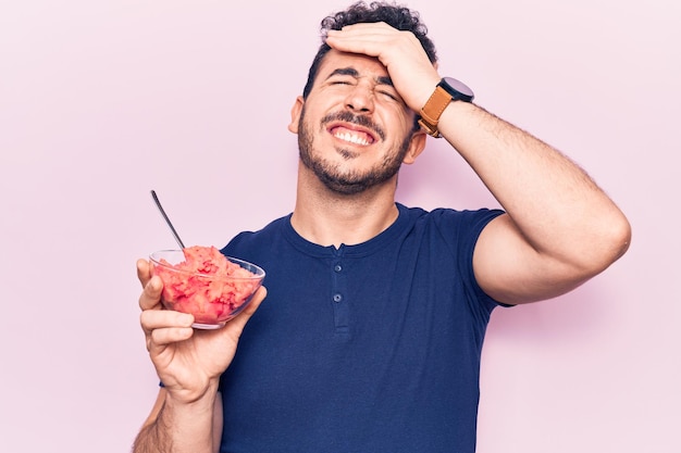 Joven hispano sosteniendo helado estresado y frustrado con la mano en la cabeza, cara sorprendida y enojada