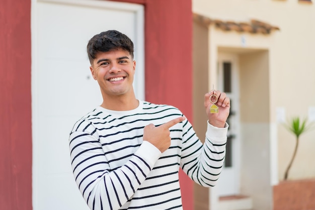 Foto joven hispano sosteniendo las llaves de casa al aire libre y apuntándolas