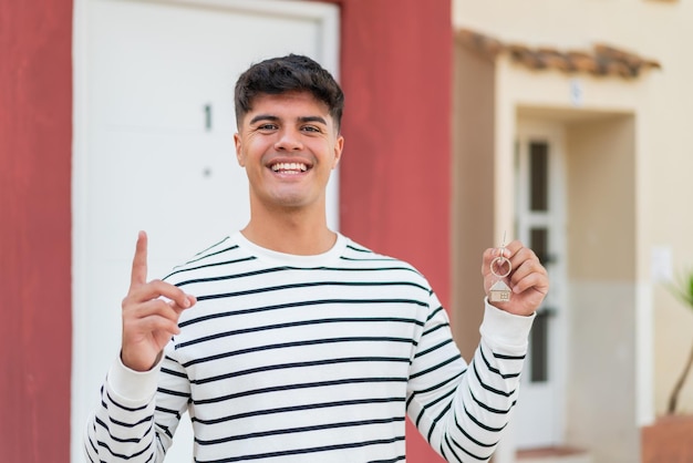 Foto joven hispano sosteniendo las llaves de la casa al aire libre señalando una gran idea