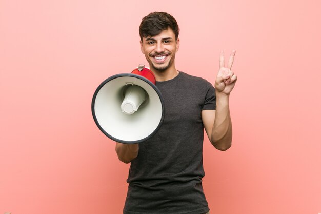 Joven hispano sosteniendo un megáfono mostrando el número dos con los dedos.