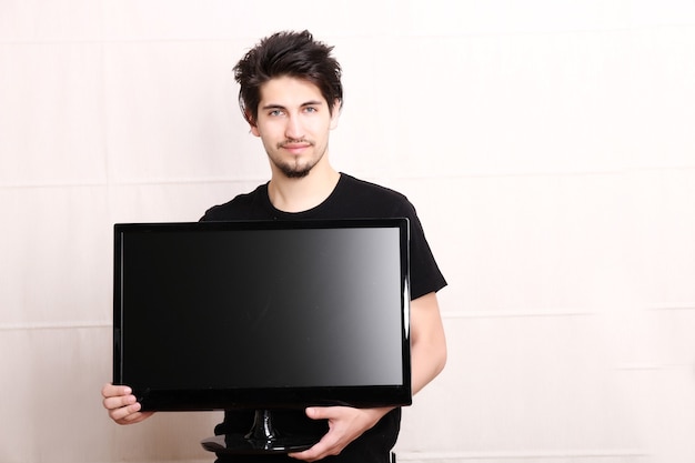 Un joven hispano sosteniendo un televisor de pantalla plana.