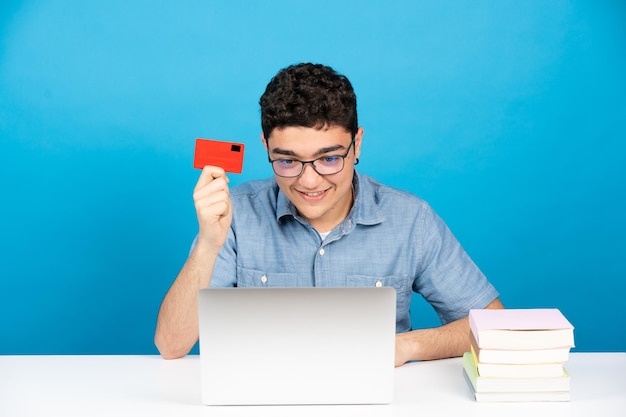 Joven hispano con tarjeta de crédito y compras en línea frente a la computadora portátil