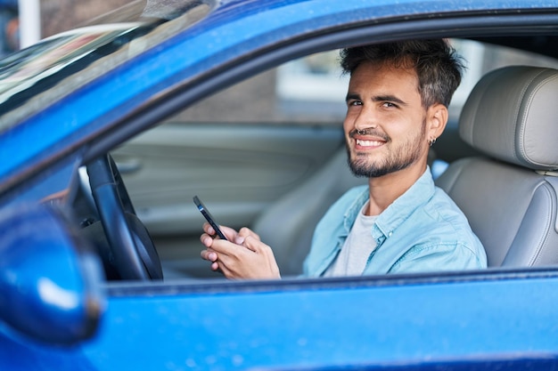 Joven hispano usando un teléfono inteligente sentado en un auto en la calle