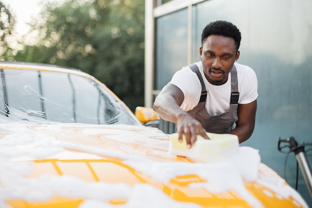Joven hombre africano atractivo lavando su auto de lujo moderno en una estación de lavado de autos de autoservicio